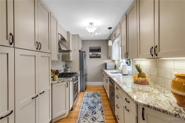 kitchen featuring wall chimney range hood, a sink, stainless steel appliances, baseboards, and tasteful backsplash