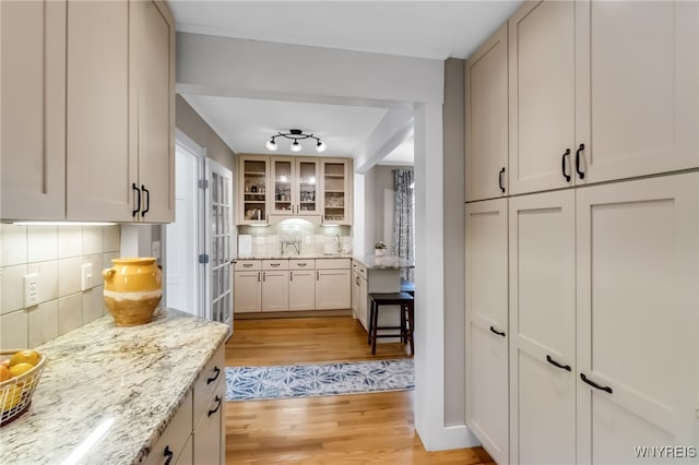kitchen featuring light wood-type flooring, backsplash, glass insert cabinets, and light stone counters