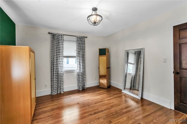 unfurnished bedroom with wood finished floors, baseboards, and a chandelier