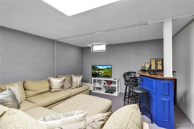 living room featuring carpet, concrete block wall, and a paneled ceiling