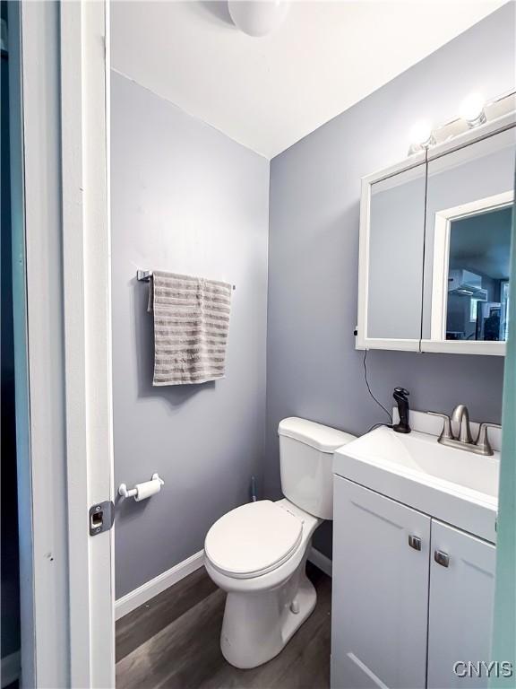 half bath featuring wood finished floors, toilet, baseboards, and vanity