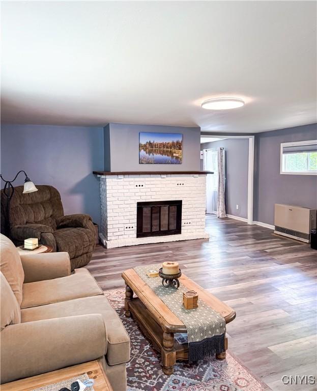 living room with wood finished floors, a brick fireplace, and baseboards