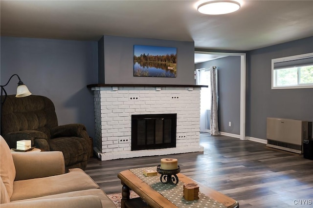 living room with dark wood-style flooring, a brick fireplace, baseboards, and heating unit