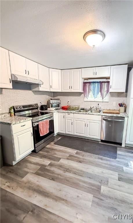 kitchen with appliances with stainless steel finishes, under cabinet range hood, a sink, dark wood-type flooring, and a textured ceiling