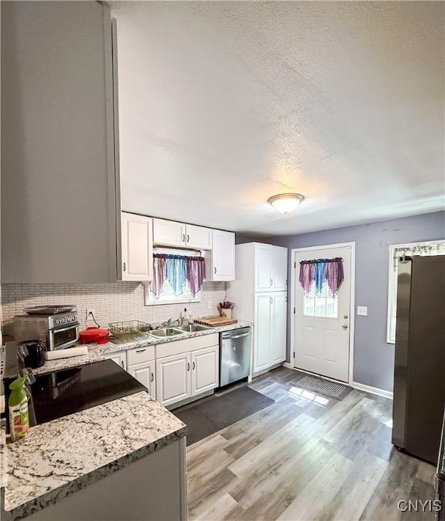 kitchen featuring a sink, stainless steel dishwasher, tasteful backsplash, white cabinets, and range