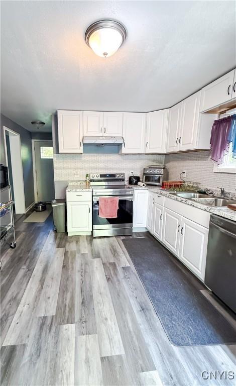 kitchen with electric stove, dishwashing machine, a sink, under cabinet range hood, and white cabinets