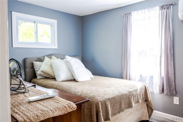bedroom with a wall unit AC, baseboards, and wood finished floors