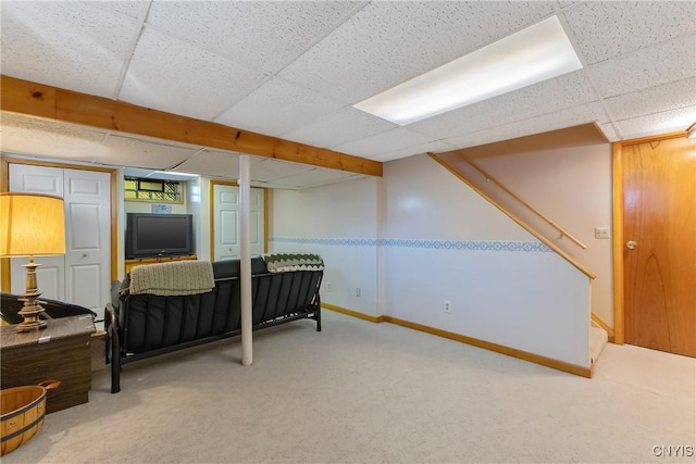 below grade area featuring a paneled ceiling, carpet, baseboards, and stairway