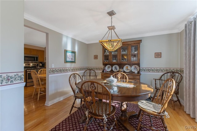 dining area with light wood-style flooring, a wainscoted wall, a chandelier, and crown molding