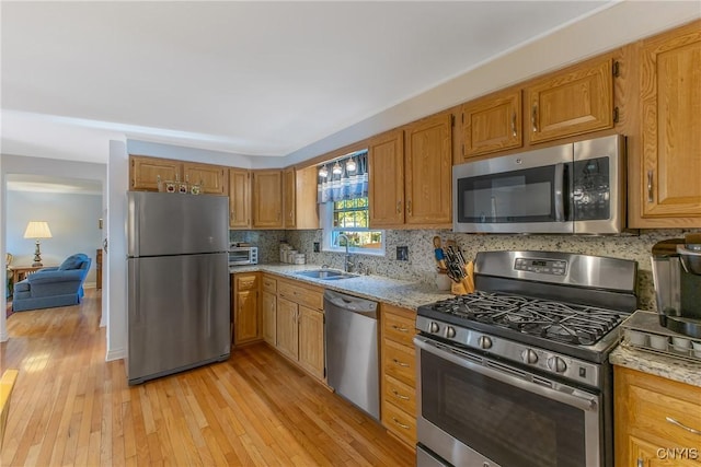 kitchen with stainless steel appliances, a sink, light wood-style flooring, light stone countertops, and backsplash