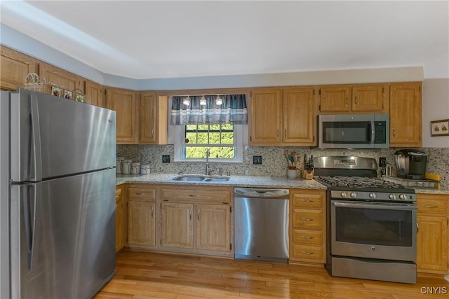 kitchen with stainless steel appliances, a sink, light stone counters, and tasteful backsplash