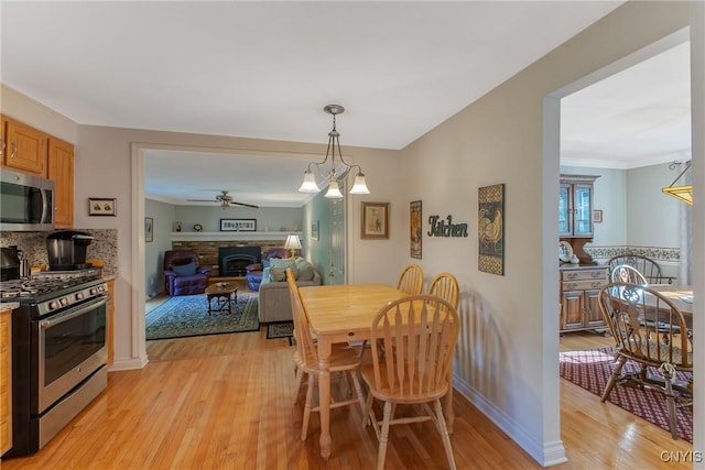 dining room featuring light wood-style floors, a fireplace, ceiling fan, and baseboards