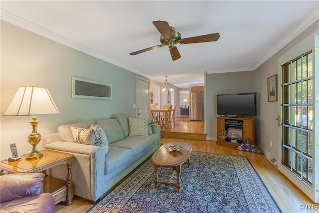 living room featuring wood finished floors, ornamental molding, ceiling fan, a chandelier, and baseboards