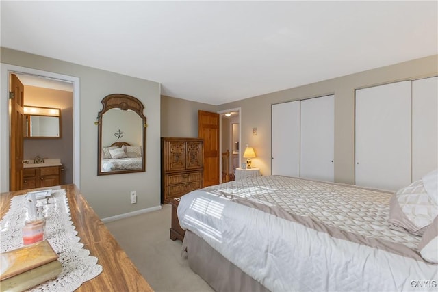 bedroom featuring two closets, carpet floors, baseboards, a sink, and ensuite bath