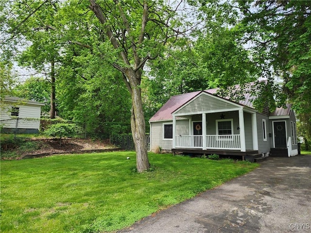 bungalow-style home featuring covered porch, a front yard, metal roof, and asphalt driveway