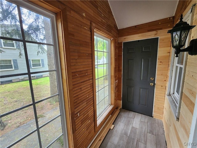foyer entrance featuring wooden walls, vaulted ceiling, and light wood-style floors