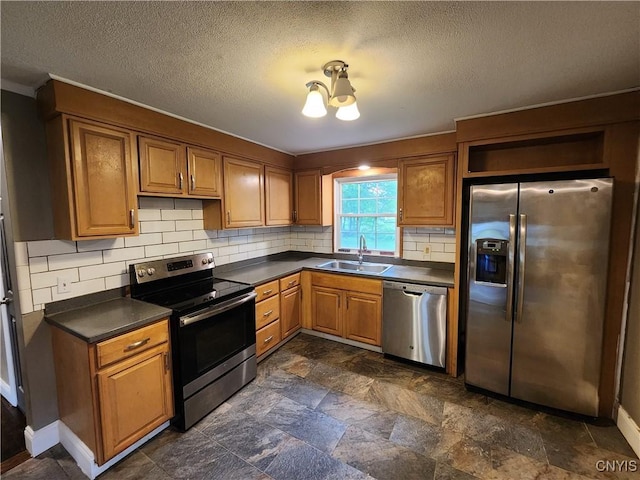 kitchen with appliances with stainless steel finishes, a sink, dark countertops, backsplash, and a textured ceiling