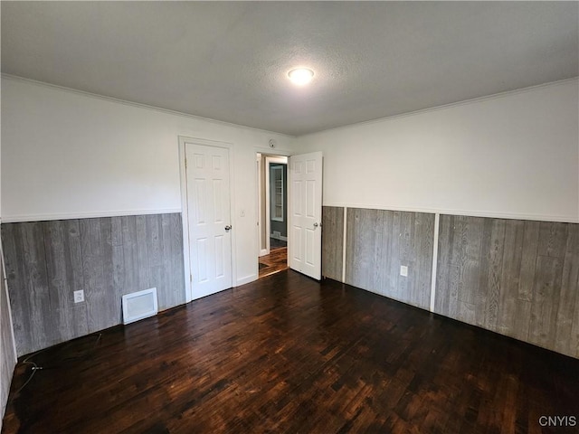 empty room with wainscoting, wood finished floors, ornamental molding, and wood walls