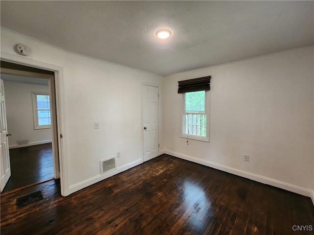 unfurnished room with dark wood-style floors, plenty of natural light, baseboards, crown molding, and a textured ceiling