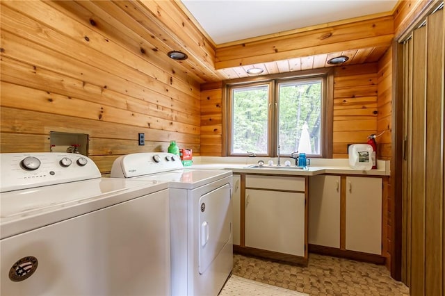 laundry room with independent washer and dryer, wooden walls, cabinet space, and light floors