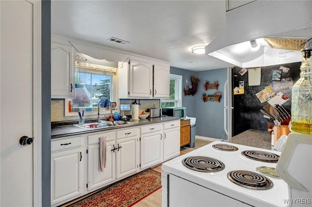kitchen featuring a sink, white electric range, stainless steel microwave, and white cabinetry