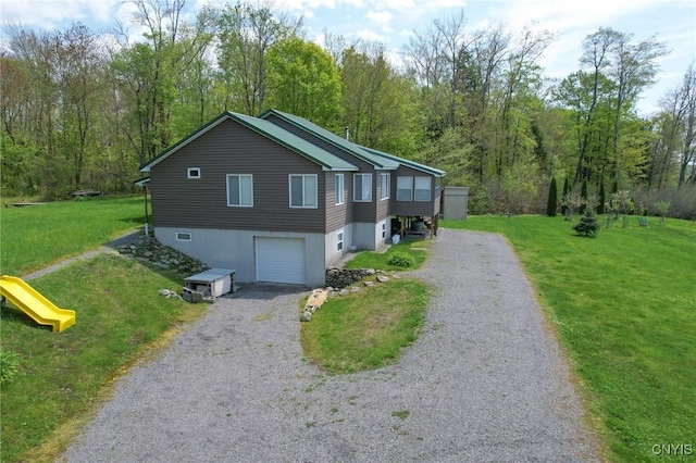 view of front facade with gravel driveway, a front yard, a garage, and a wooded view