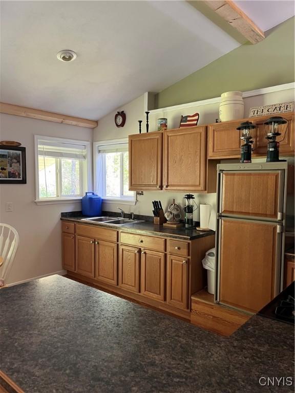 kitchen with a sink, lofted ceiling, dark countertops, refrigerator, and brown cabinetry