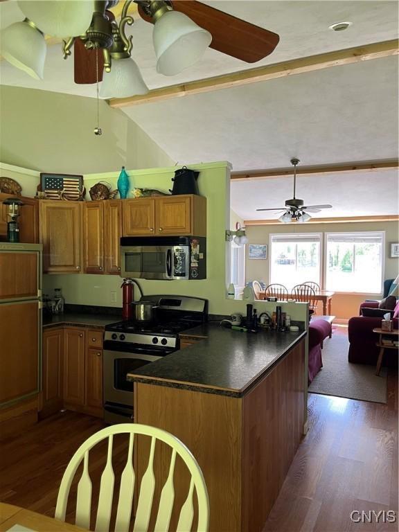 kitchen with stainless steel appliances, ceiling fan, dark wood-style flooring, brown cabinetry, and vaulted ceiling