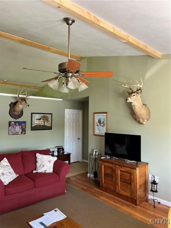 living room featuring wood finished floors, baseboards, beamed ceiling, and a ceiling fan