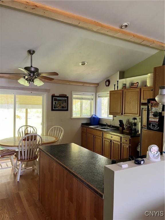 kitchen featuring dark countertops, a sink, vaulted ceiling, and brown cabinets