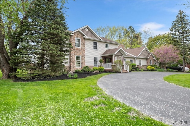 view of front of home with stone siding, curved driveway, a front yard, and covered porch