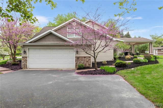 view of front of home with stone siding, driveway, a garage, a front yard, and ceiling fan