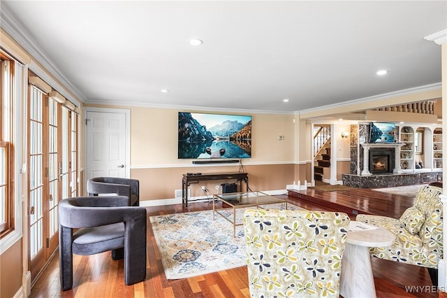 living room featuring wood finished floors, baseboards, a fireplace, crown molding, and stairs