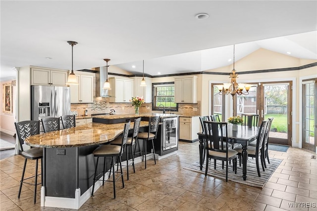 kitchen featuring stainless steel fridge, wall chimney range hood, a spacious island, backsplash, and lofted ceiling