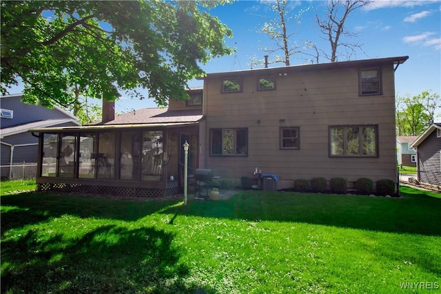 rear view of house with a sunroom, a yard, and a chimney