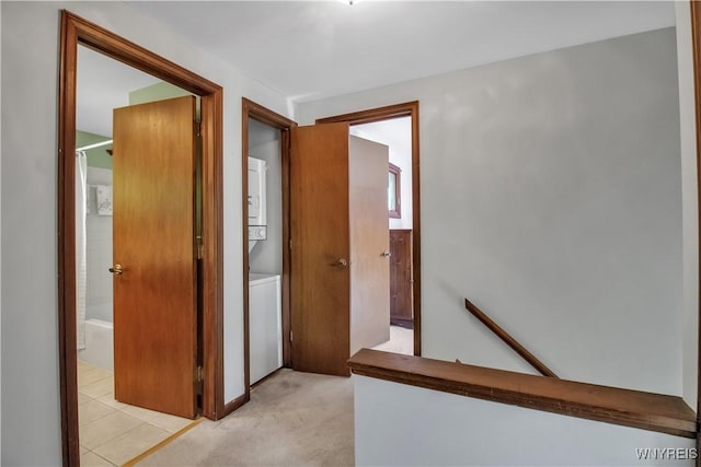 hallway with stacked washer and clothes dryer, an upstairs landing, and light carpet