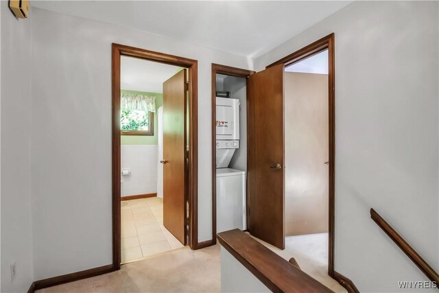 hallway featuring stacked washer / drying machine, light carpet, baseboards, and light tile patterned floors
