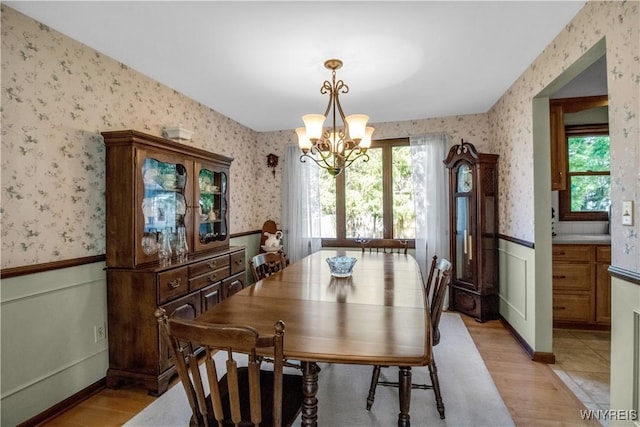 dining space featuring wallpapered walls, wainscoting, a chandelier, and light wood finished floors