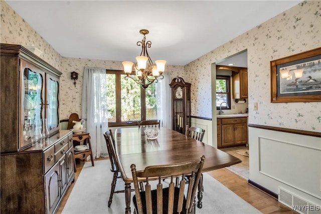 dining room with wallpapered walls, wainscoting, a chandelier, plenty of natural light, and light wood finished floors