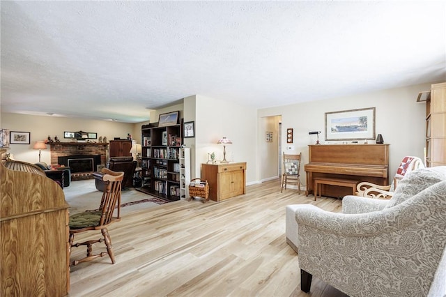 living room with light wood-style flooring, a brick fireplace, and a textured ceiling