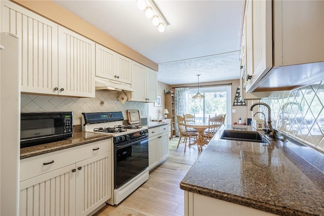 kitchen featuring gas range oven, a sink, black microwave, under cabinet range hood, and tasteful backsplash
