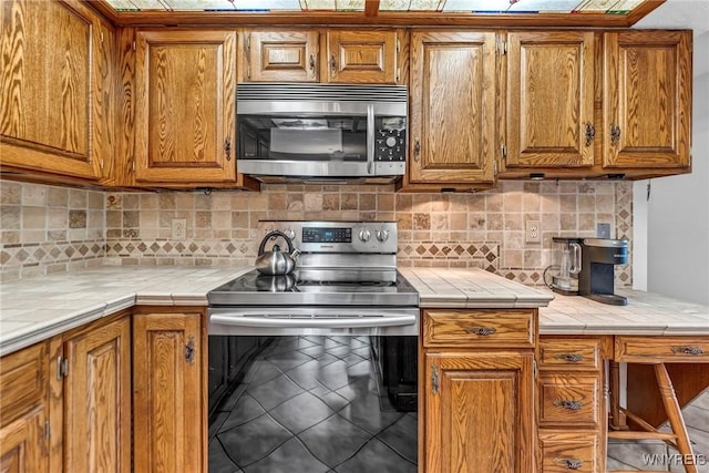 9811 Deer Creek Rd, Genesee, NY 14770 - kitchen with stainless steel appliances, brown cabinets, tile countertops, and backsplash