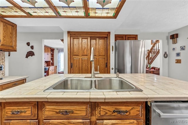 9811 Deer Creek Rd, Genesee, NY 14770 - kitchen with stainless steel appliances, a sink, brown cabinetry, tile countertops, and decorative backsplash