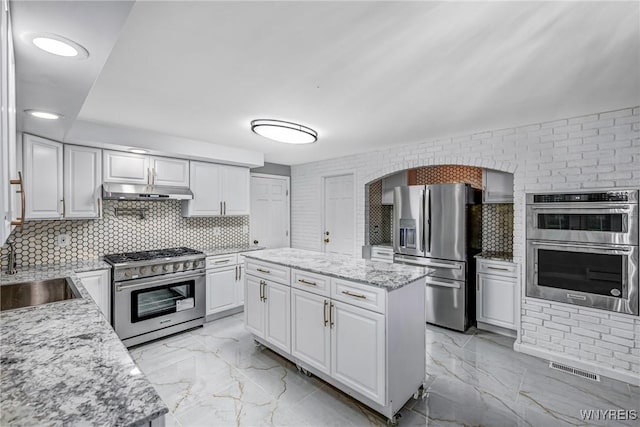 kitchen featuring appliances with stainless steel finishes, a sink, under cabinet range hood, white cabinetry, and light marble finish flooring