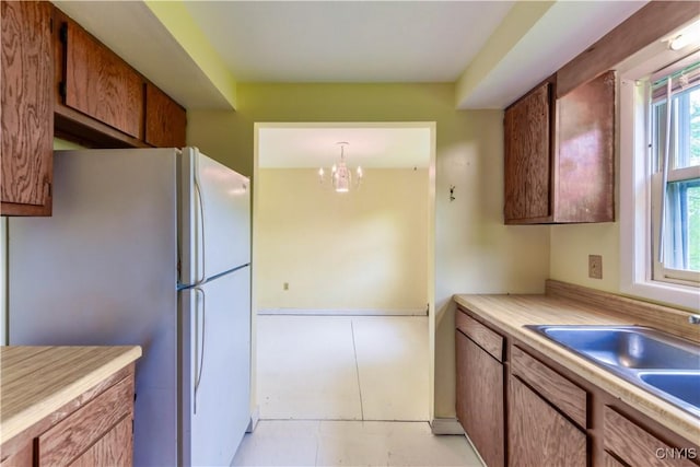 kitchen featuring freestanding refrigerator, light countertops, a chandelier, a sink, and brown cabinets