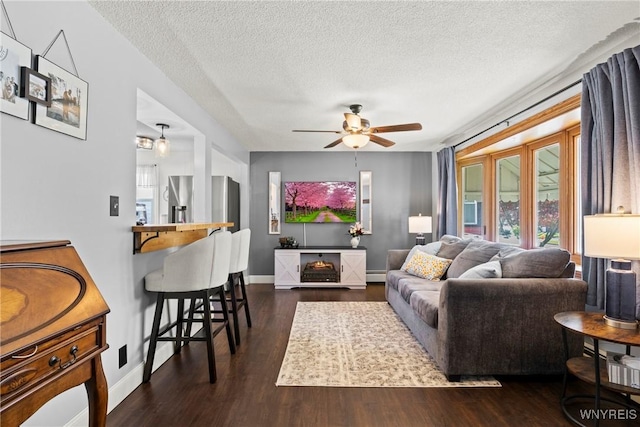 living room with a textured ceiling, a ceiling fan, dark wood-style floors, and baseboards