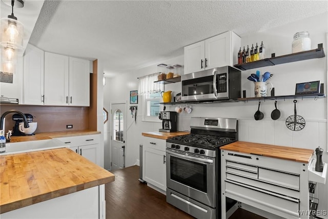 kitchen with wood counters, appliances with stainless steel finishes, open shelves, a sink, and dark wood finished floors