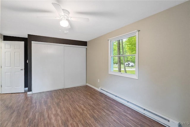 unfurnished bedroom with baseboard heating, wood finished floors, a closet, a ceiling fan, and baseboards