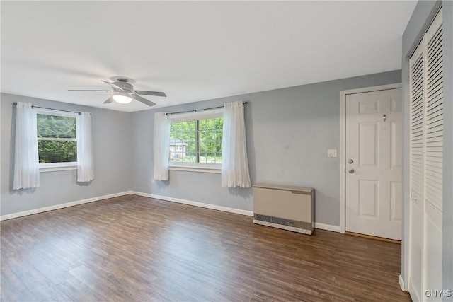 empty room with heating unit, wood finished floors, a ceiling fan, and baseboards