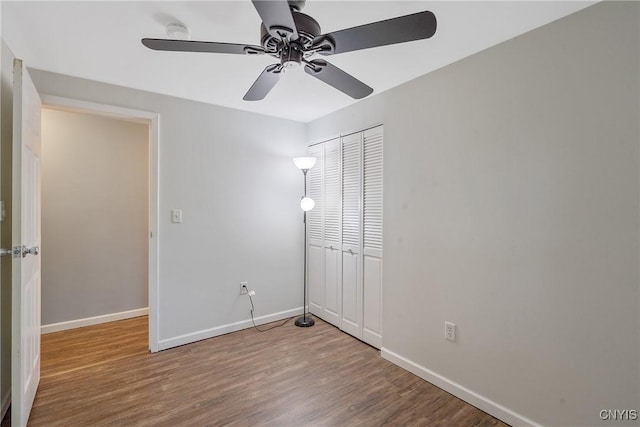 unfurnished bedroom with baseboards, wood finished floors, a closet, and a ceiling fan
